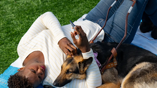 A person laying down on a picnic blanket with their service dog