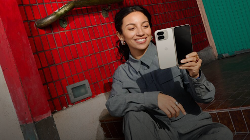 Une femme souriante assise sur une chaise, regardant un téléphone pliable ouvert dans sa main.