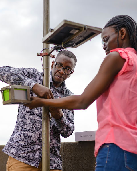 Engineer Bainomugisha und ein Teamkollege beim Installieren eines Sensors auf einem Dach im geschäftigen Kampala