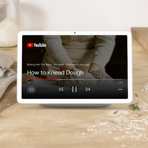 A tablet sits on a charging dock, playing a YouTube video titled, 'How to knead dough'.