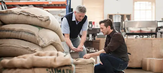 Dos hombres mirando granos de caf� en un taller.