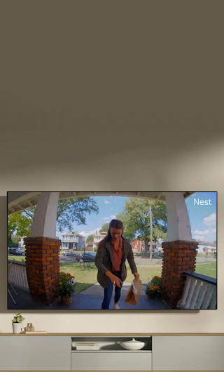 A TV in a living room showing a delivery person standing on a stoop waving to the doorbell camera.