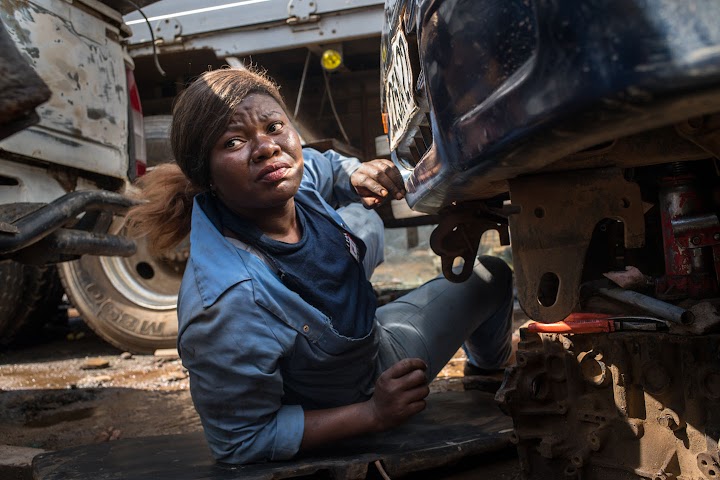 Princesse trabajando debajo de un auto vestida con un overol azul