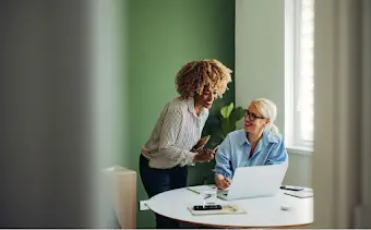 2 vrouwen staan gebogen over een laptop en bespreken hun werk.