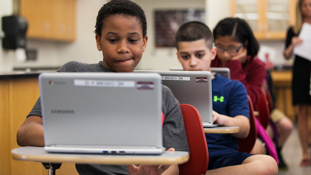 Two young boys in a classroom working on their laptops