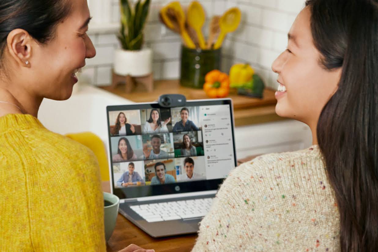 Dos personas sentadas en una cocina se sonr�en mientras participan en una llamada de Google�Meet.