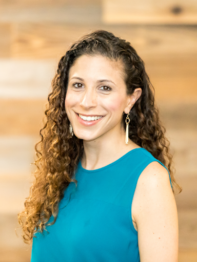 Portrait of a smiling woman with long curly hair, dangling earrings, and a teal blue blouse