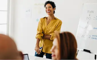 Uma mulher na frente de uma sala realizando uma sess�o de trabalho em lousa interativa com sua equipe.