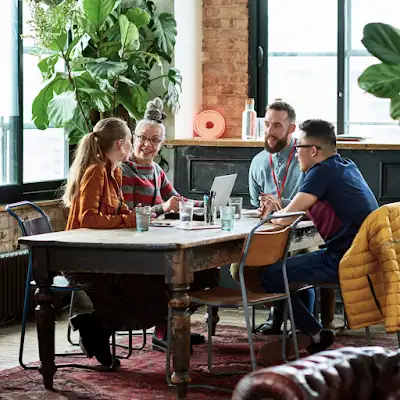 Four coworkers gather around a conference table in a lush office setting surrounded with greenery.