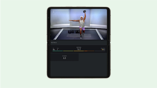 A foldable phone displays a gym trainer lifting weights on the top half of the screen with health metrics on the bottom of the screen.