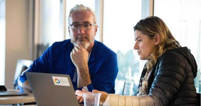 Two people sit at a table and engage with a laptop.