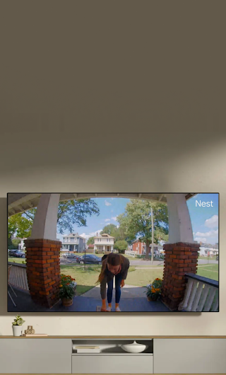 A TV in a living room showing a delivery person standing on a stoop waving to the doorbell camera.