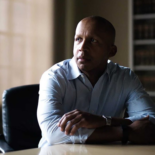 Black man in a dress shirt sitting at a desk with his arms crossed