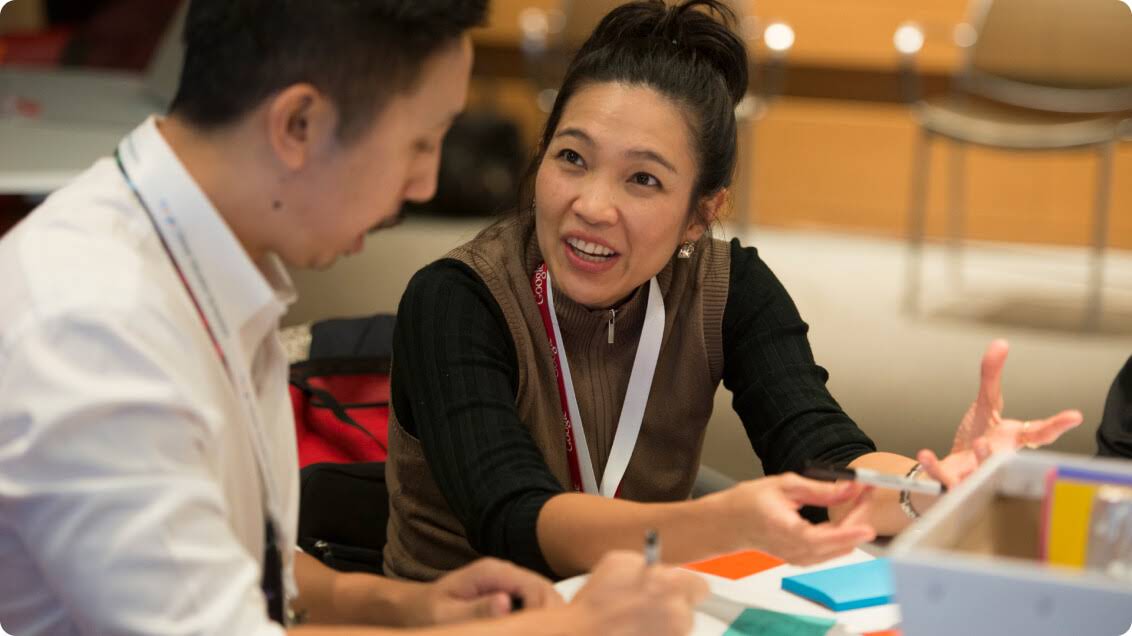 Two people engage in discussion while holding markers and writing on sticky notes.