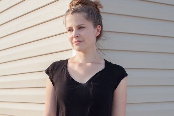 Portrait of Thoka Maer, an art director on the Google Doodles team. She’s standing against a wall wearing a black shirt and has her hair up in a bun.