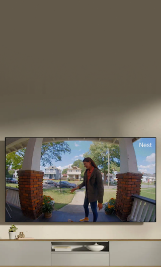 A TV in a living room showing a delivery person standing on a stoop waving to the doorbell camera.