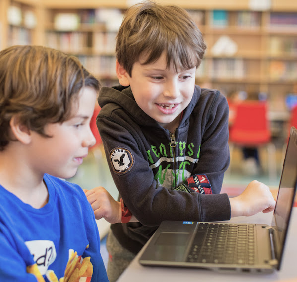 Two young students work on a laptop.