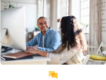 Dos personas trabajando juntas con un monitor grande delante.