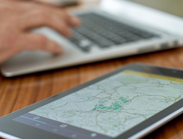 Person working on laptop with a map on a tablet