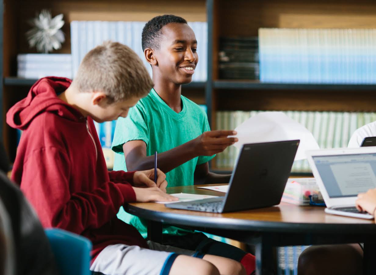 Uno studente tiene in mano un foglio di carta, mentre accanto a lui un altro studente � al lavoro davanti a un Chromebook.