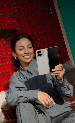 Uma mulher sorridente sentada em uma cadeira olhando para um smartphone dobr�vel aberto na m�o.