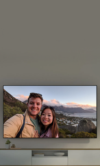 A TV in a living room casting an image from a phone of a couple in front of a mountain landscape.