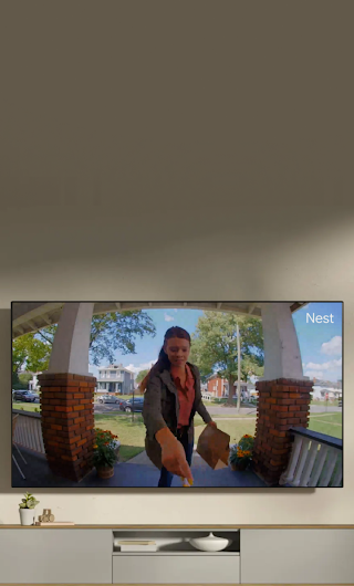 A TV in a living room showing a delivery person standing on a stoop waving to the doorbell camera.