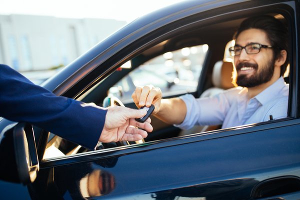 Person hands car keys to man sitting inside a car.