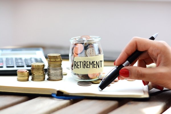 Hand holds pen near jar of coins labeled Retirement.