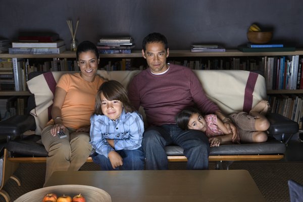 Family sitting on a couch and watching TV in the dark.