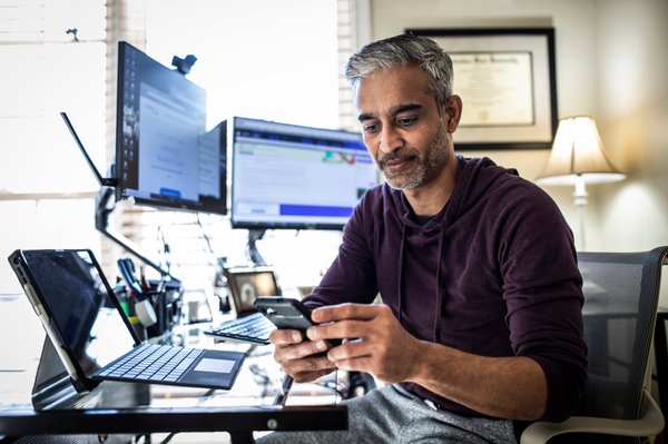 Person using phone at desk with multiple computer monitors.