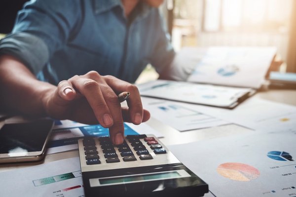 A person using a calculator with financial charts on the desk.