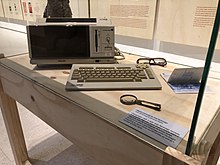 An old computer, accompanied by a pair of glasses and a loupe.