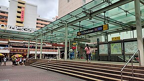 Exit C of Chinatown station, a covered glass entrance atop a short set of stairs in a brick plaza. The covered entrance is surrounded by tall buildings in the background.