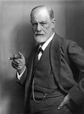 photograph of a balding man with a beard; holding a cigar and wearing a suit