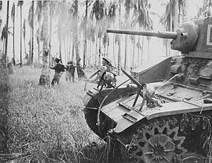 7 January 1943. Australian forces attack Japanese positions near Buna. Members of the 2/12th Infantry Battalion advance as Stuart tanks from the 2/6th Armoured Regiment attack Japanese pillboxes. An upward-firing machine gun on the tank sprays treetops to clear them of snipers. (Photographer: George Silk).