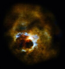 Space telescope image of star Mira A, observed from Earth. A cloud of gas and dust is illuminated by a whitish light concentrated at center of image; some hints of blue and yellow are visible near the center. The clouds obscure direct view of the star, and are front- and backlit by its light depending on their orientations, with some of the thick dark clouds between the star and viewer standing out due to partially obscuring the light from the star. The image darkens rapidly towards its edges as the clouds absorb and scatter the light, first becoming increasingly dimmer and redder, and closer to the edges the image becomes more or less completely black.