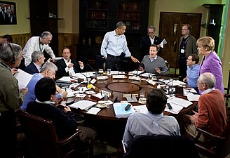 Líderes mundiais na Cúpula do G8 de 2012 . (Sentido horário) Barack Obama (em pé), Cameron, Medvedev, Merkel, Van Rompuy, Barroso, Noda, Monti, Harper, e Hollande.