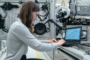 Young woman systems engineer working at lab facility on a laptop surrounded by equipment