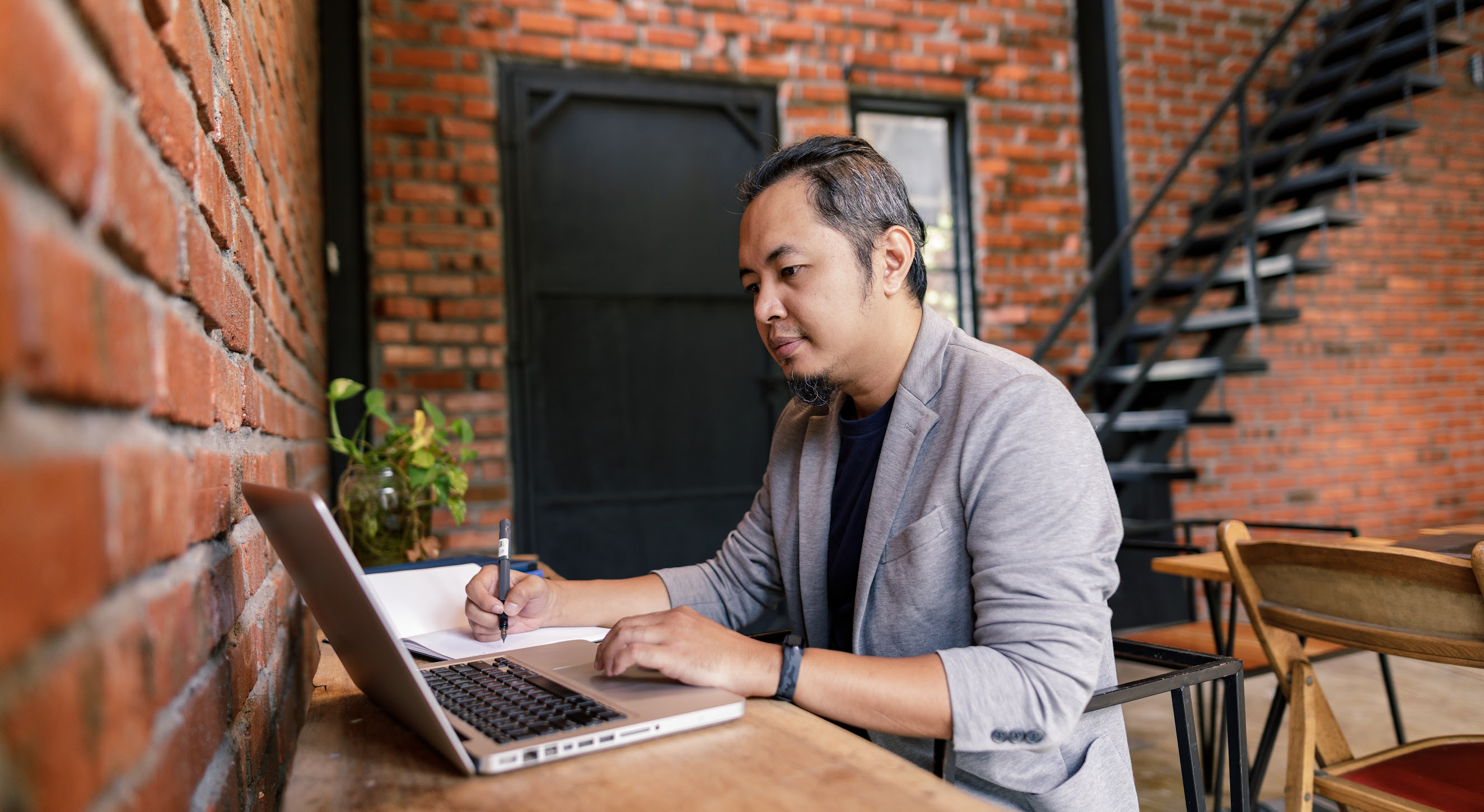 Portrait of a man writing down details from his laptop.