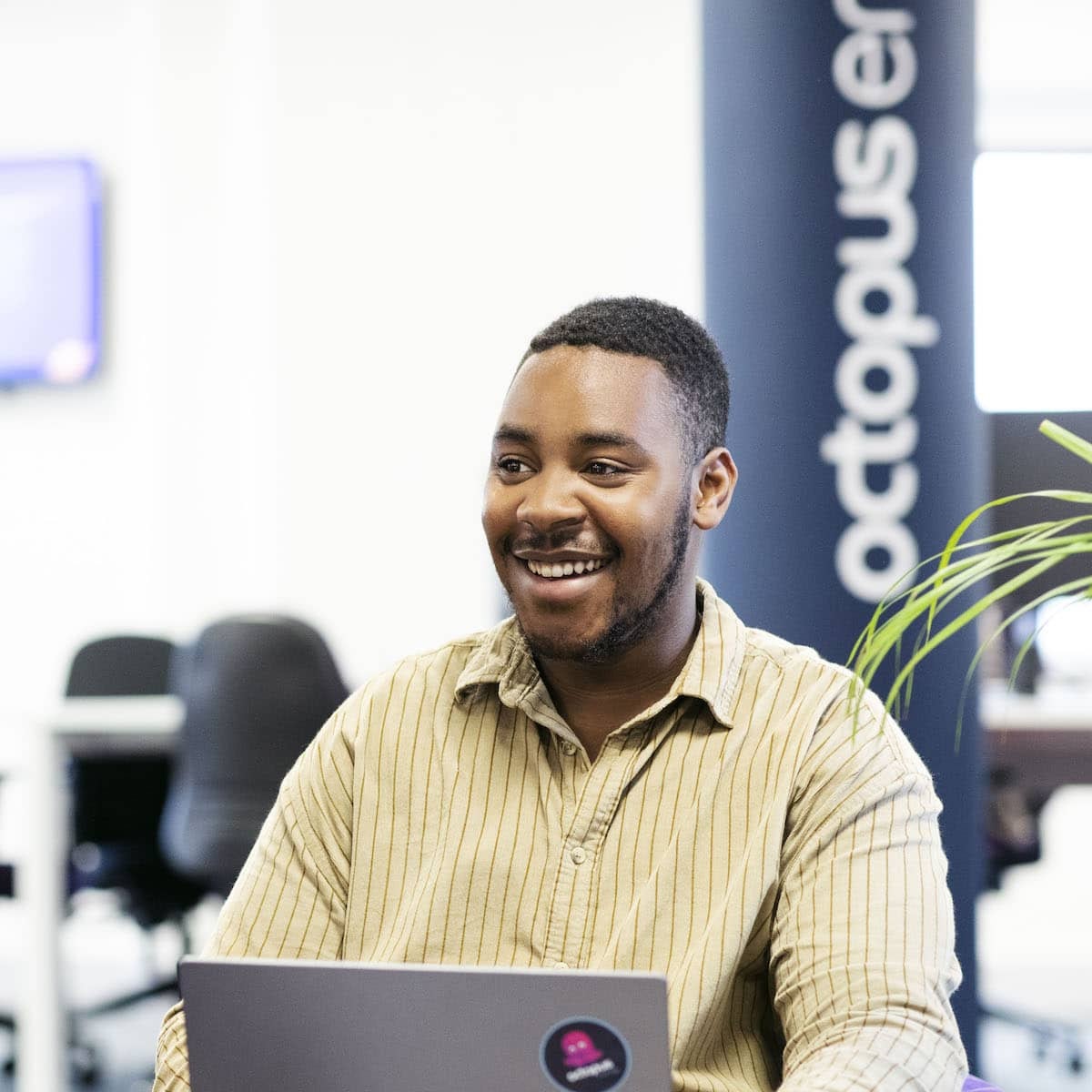 Man sitting in an Octopus Energy office, smiling with a laptop in front of him.