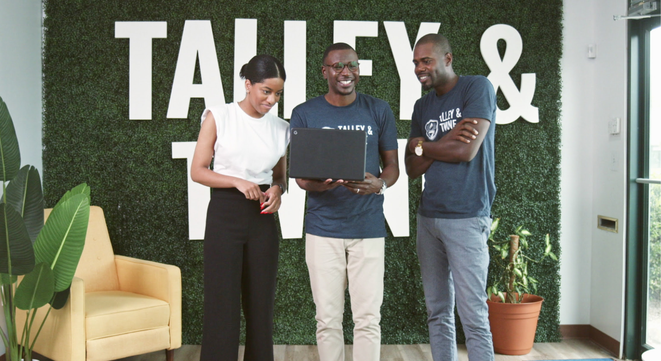 Three Talley & Twine employees standing together in front of the Talley & Twine sign in the office