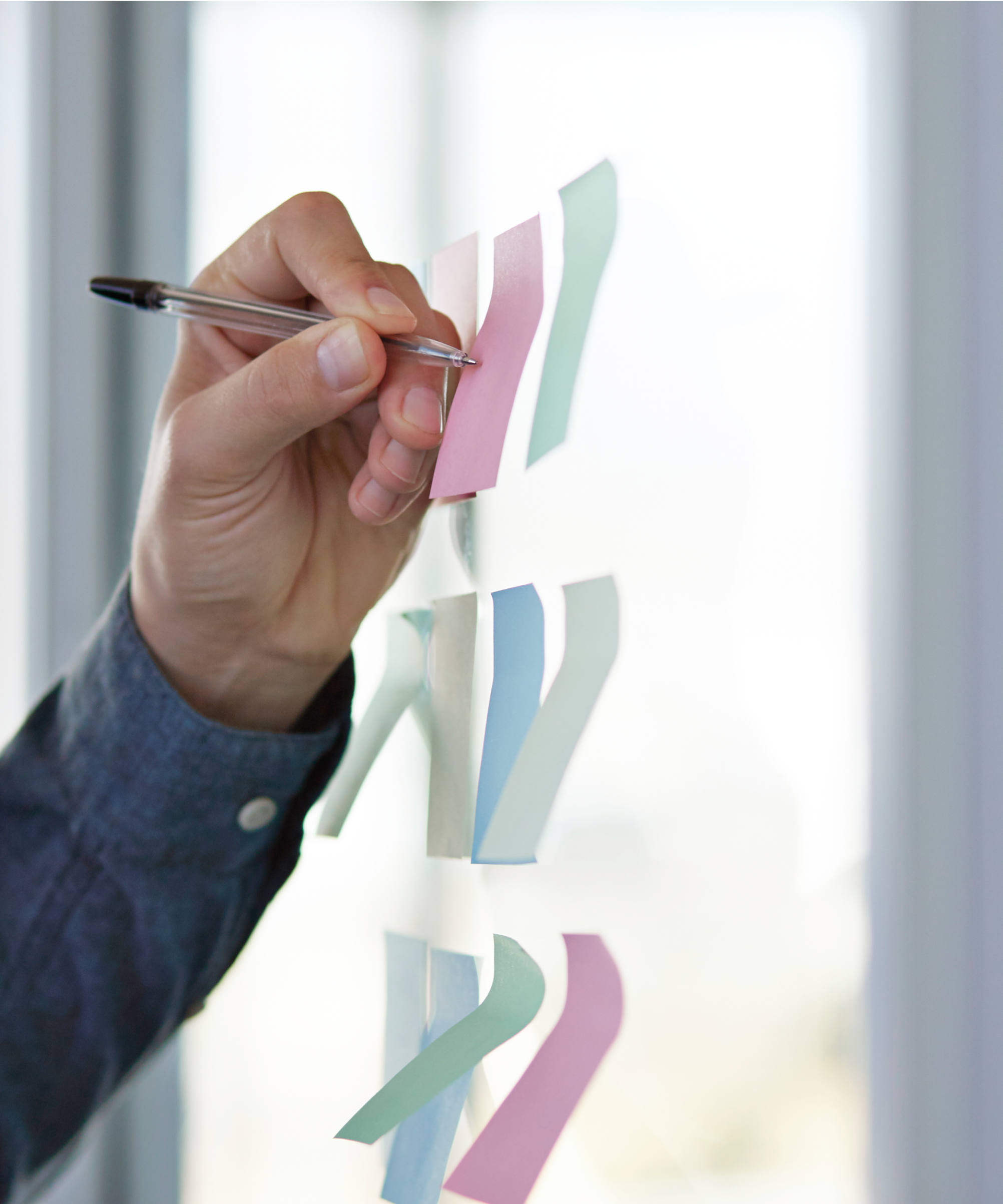 A person’s left arm writes on sticky notes that are placed on a glass wall.