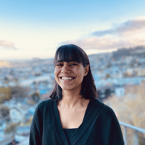 Photograph of a woman with short black hair and brown skin smiling to camera.