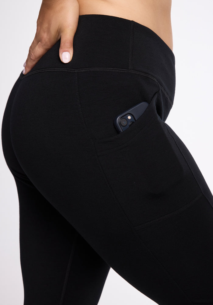 Close-up of a person wearing Woolx Frost Duralite� Leggings - Black with their hand resting on the hip. A smartphone is partially visible in the pocket on the side of these warmest leggings.