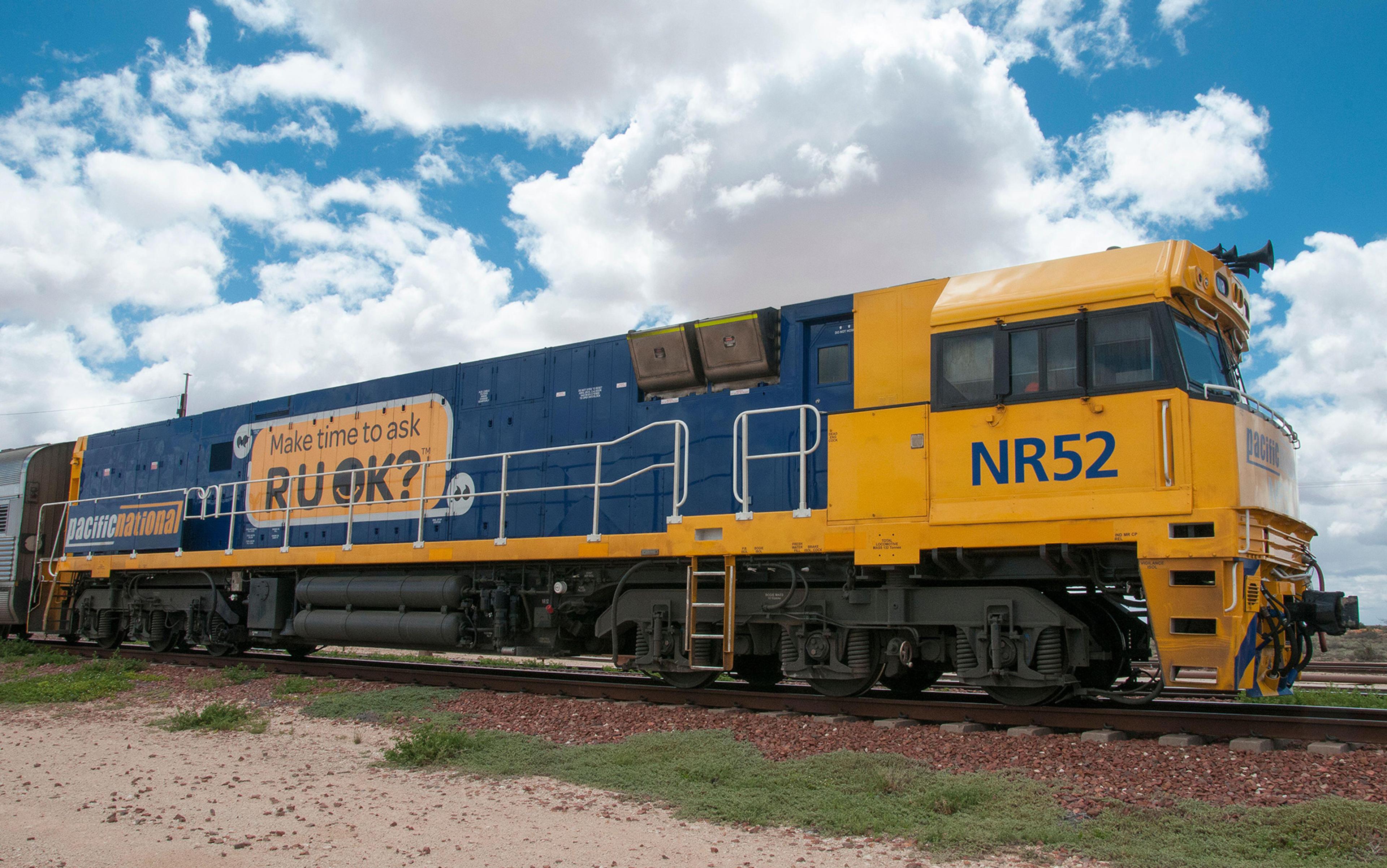 A Pacific National train engine in yellow and blue with “Make time to ask R U OK?” message on its side.