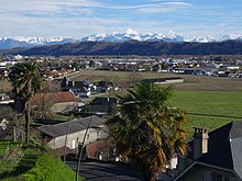 Photographie en couleurs d'une ville et de champs, avec en fond des montagnes.