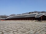 Very wide and narrow building with a prominent roof and red columns.