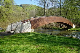 Pont en bois et béton enjambant une rivière en lisière de forêt.