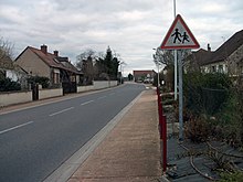 Traversée de la route départementale dans le village. Un panneau indique un endroit fréquenté par les enfants.